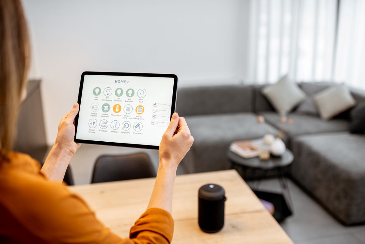 Žena drží tablet s funkciami na ovládanie smart domácnosti.