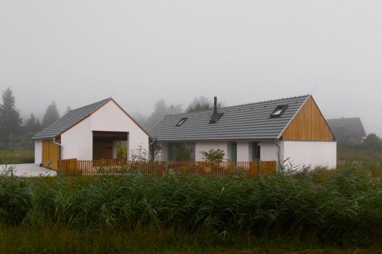 Dom obklopený zeleňou s modernou bielou a drevenou fasádou.