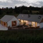 Exteriér domu a hospodárskej budovy počas večera s moderným dizajnom a sedlovou strechou.