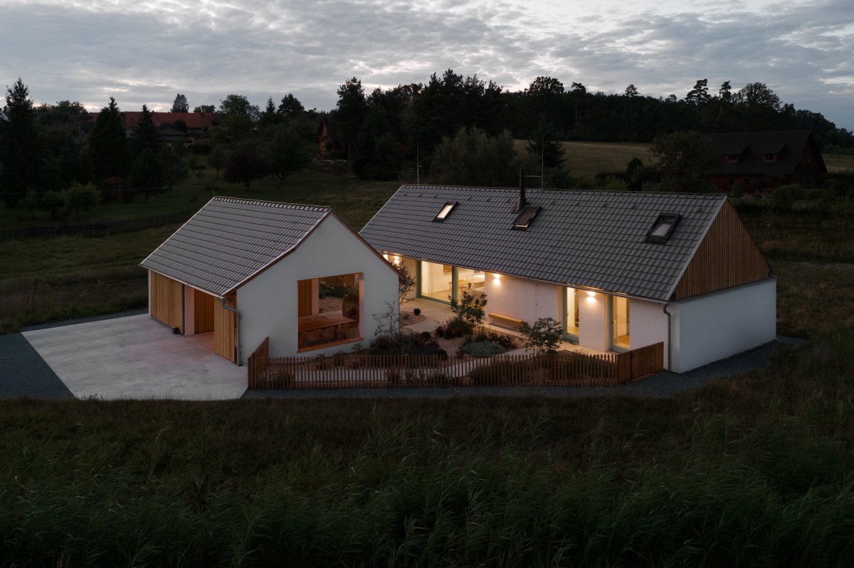 Exteriér domu a hospodárskej budovy počas večera s moderným dizajnom a sedlovou strechou.
