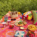 Pestré piknikové posedenie s jasnými vankúšmi, nápojmi a občerstvením na vzorovanom koberci.