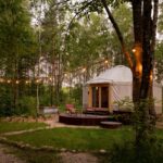 Jurta pre glamping uprostred lesa so svetielkami a terasou.