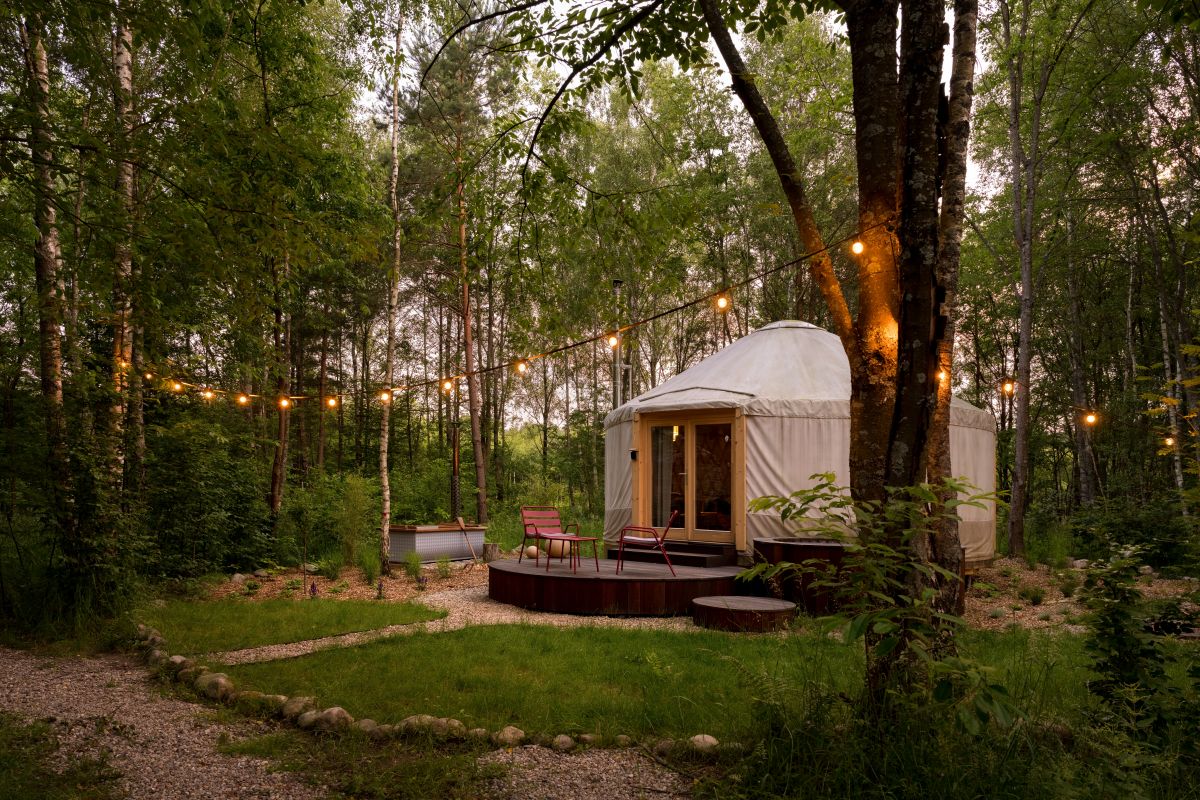 Jurta pre glamping uprostred lesa so svetielkami a terasou.