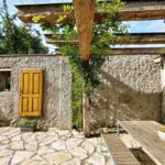 Pergola v rohu záhrady s drevenými trámami a kamenným oplotením.