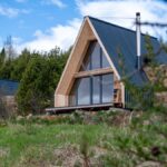 Tri tiny houses s presklenou fasádou a áčkovým tvarom v prírode pod lesom.