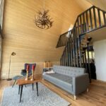 Obývačka v tiny house s drevom na stenách a schodmi na spaciu galériu.