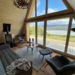 Moderná šedá sedačka a kreslá pri presklenej fasáde tiny house s výhľadom na krajinu islanduI