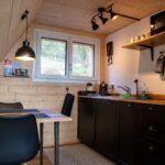 Kuchyňa spojená s jedálňou s čiernou linkou a čiernymi stoličkami v tiny house.