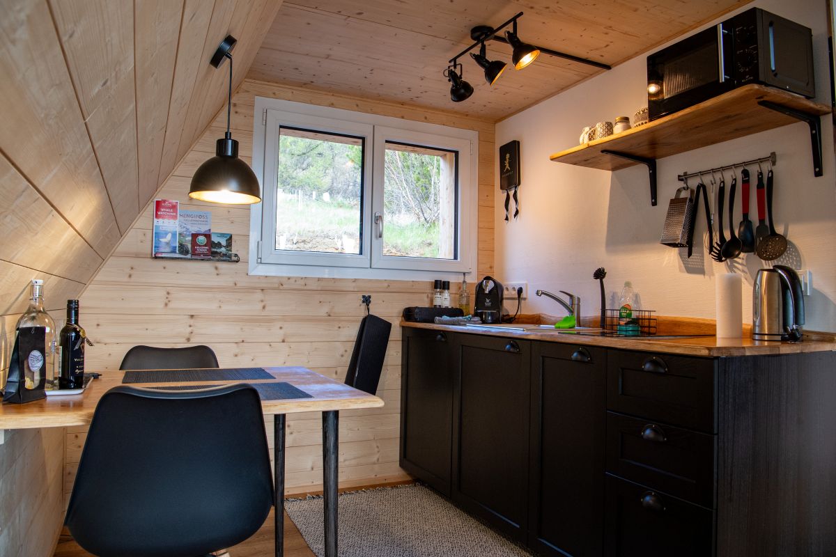 Kuchyňa spojená s jedálňou s čiernou linkou a čiernymi stoličkami v tiny house.