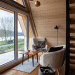 Pohodlné sedenie pri presklenej fasáde s výhľadom na jazero a les v drevostavbe tiny house.