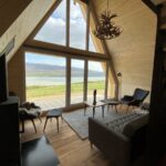 Výhľad na krajinu cez presklenú fasádu tiny house s útulným sedením v interiéri.