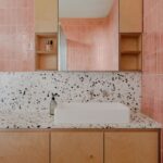 Kúpeľňa s ružovým vertikálnym a terrazzo obkladom a umývadlom.