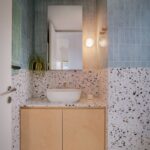 Kúpeľňa s modrými vertikálnymi obkladačkami a terrazzo obkladom, umývadlom a drevenou skrinkou.
