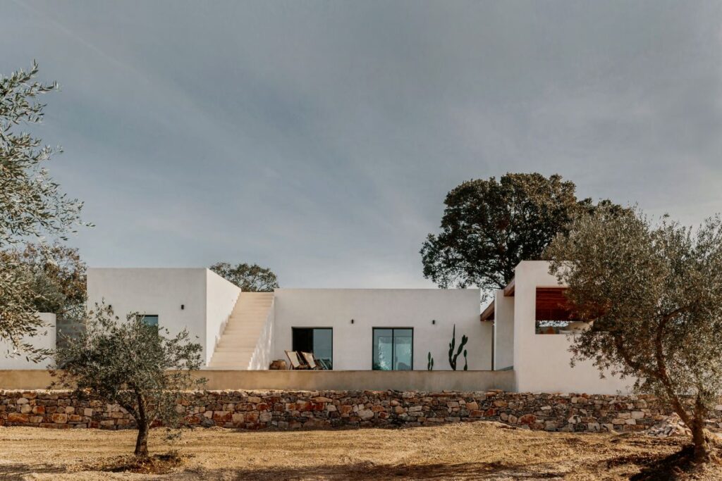 Minimalistická biela vila s vonkajším schodiskom, lemovaná kamenným múrom.