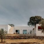 Minimalistická biela vila s vonkajším schodiskom, lemovaná kamenným múrom.