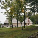 Vila s kamennou a drevenou fasádou, obklopenú vysokými stromami a trávnatou záhradou.