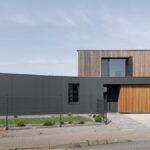 Moderný rodinný dom s tmavosivou fasádou a dreveným obkladom, s veľkými oknami a rovnou strechou.