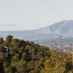 Biely dom schovaný v zeleni, s panoramatickým výhľadom na kopce a okolité mesto.
