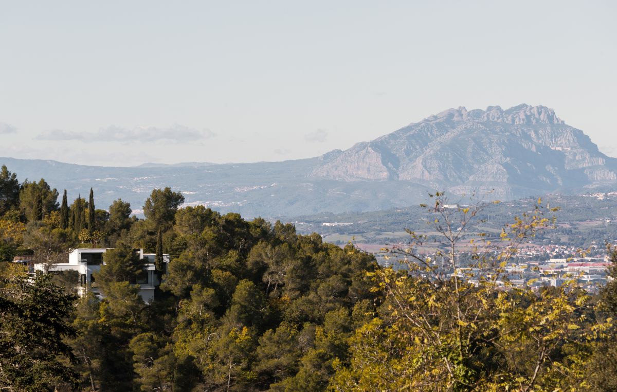 Biely dom schovaný v zeleni, s panoramatickým výhľadom na kopce a okolité mesto.