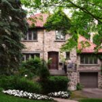 Rodinný dom s kamennou fasádou a červenou strechou, obklopený zeleňou.