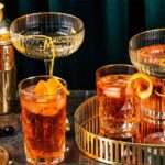 Poháre s oranžovým koktailom a zlatým šejkrom v art deco štýle.