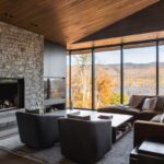 Obývacia izba s krbom obloženým prírodným kameňom, dreveným stropom a veľkými oknami s výhľadom.