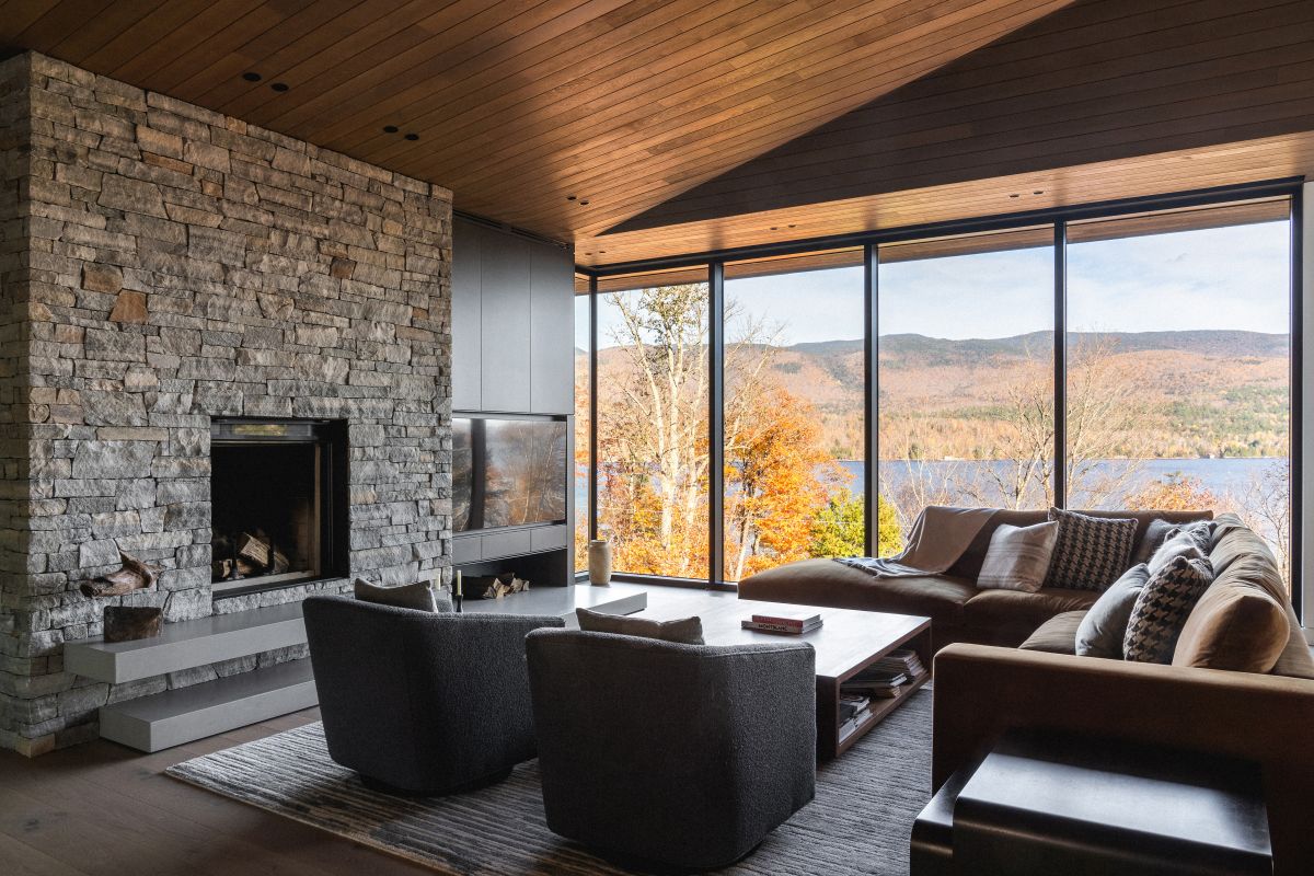 Obývacia izba s krbom obloženým prírodným kameňom, dreveným stropom a veľkými oknami s výhľadom.