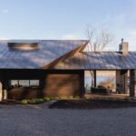 Moderný prízemný dom so šikmou plechovou strechou, kamennou fasádou a drevenou terasou s výhľadom na jazero.