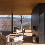 Vonkajšia terasa s drevenou podlahou a moderným ratanovým nábytkom s výhľadom na jazero a hory.