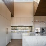 Moderná biela kuchyňa s mramorovým ostrovčekom a bronzovými batériami.