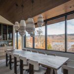 Jedáleň s masívnym dreveným stolom, dizajnovými lampami a veľkými oknami s výhľadom na jesennú krajinu.
