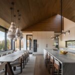 Biela kuchyňa s mramorovým ostrovčekom a jedálenský priestor s dreveným stolom a šikmým dreveným stropom.