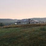 Predĺžený moderný rodinný dom s drevenou fasádou a terasou na rozľahlej lúke.