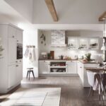 Biela vidiecka kuchyňa s presklenými skrinkami, drevenou podlahou a pracovnou doskou s viditeľnými drevenými trámami na strope.