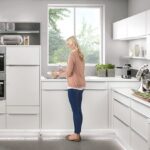 Biela lesklá moderná kuchyňa s bielym nábytkom, nerezovými vstavanými spotrebičmi a bodovým LED osvetlením pod linkou.