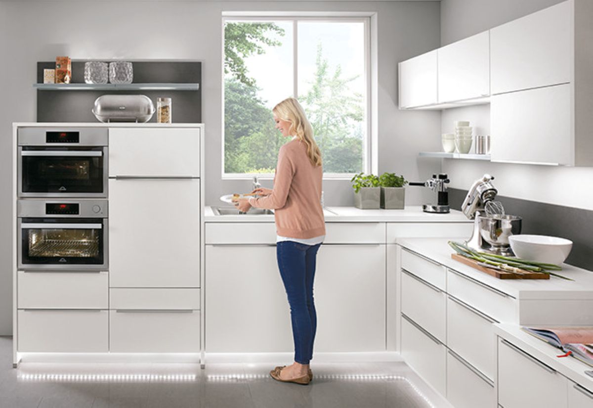 Biela lesklá moderná kuchyňa s bielym nábytkom, nerezovými vstavanými spotrebičmi a bodovým LED osvetlením pod linkou.