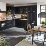 Rohová čierna kuchyňa v škandinávskom štýle s tehlovou stenou, drevenou pracovnou doskou a jedálenským kútom s ratanovým lustrom.