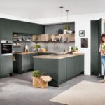 Priestranná kuchyňa v tmavej zelenej farbe s ostrovčekom, drevenými otvorenými policami a neutrálnou šedou podlahou a bielymi stenami.