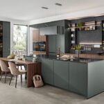 Kuchyňa v tmavozelenej farbe s ostrovčekom, integrovaným jedálenským stolom z dreva a čiernou kamennou stenou.