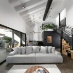 Moderná obývačka s bielym trámovým stropom, veľkou šedou sedačkou a presklenou stenou s posuvnými dverami vedúcou na terasu.