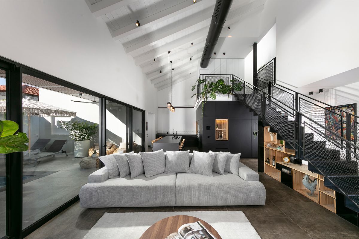 Moderná obývačka s bielym trámovým stropom, veľkou šedou sedačkou a presklenou stenou s posuvnými dverami vedúcou na terasu.