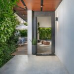 Betónový vchod vedúci do interiéru a na drevenú terasu s vonkajším posedením.