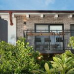 Balkón s čiernym perforovaným zábradlím a tehlovou fasádou domu.