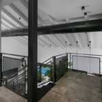 Galéria na poschodí s tmavou betónovou podlahou a čiernym kovovým zábradlím.