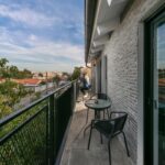 Úzky balkón s tmavou dlažbou a čiernym zábradlím s posedením pre dve osoby.