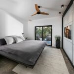 Moderná spálňa s tmavosivou posteľou, vysokými bielymi skriňami a posuvnými dverami na terasu.