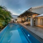 Exteriér domu s bazénom šedou dlažbou a drevenou terasou.