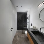 Moderná kúpeľňa s čiernym kamenným umývadlom na drevenej skrinke a sprchovým kútom s tmavou dlažbou.