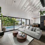 Otvorená obývačka s vysokým bielym trámovým stropom, výhľadom na bazén a čiernou kuchynskou časťou s galériou.