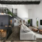 Industriálno-moderný interiér s čiernou kuchynskou linkou, kovovým schodiskom a sivou sedačkou v priestore s vysokým bielym stropom.